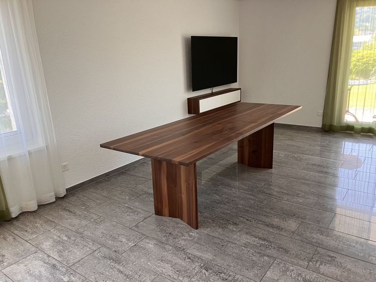 Moderner Holztisch in elegantem Raum mit Steinboden und TV-Wandinstallation.