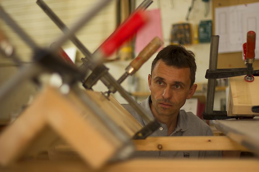 Ein Mann arbeitet konzentriert in einer Holzwerkstatt mit Klemmen und Holzbrettern.