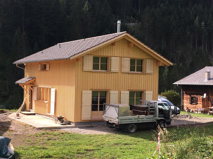 Zweistöckiges Holzhaus mit LKW davor in ländlicher Umgebung.