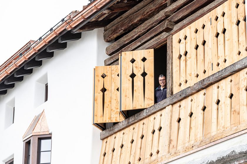 Ein Mann schaut aus einem modernen Holzfenster in einem traditionellen Gebäude.