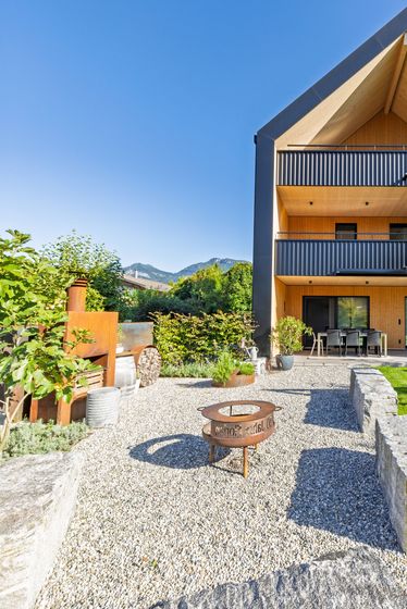 Modernes Holzgebäude mit Garten im Vordergrund bei klarem Himmel.