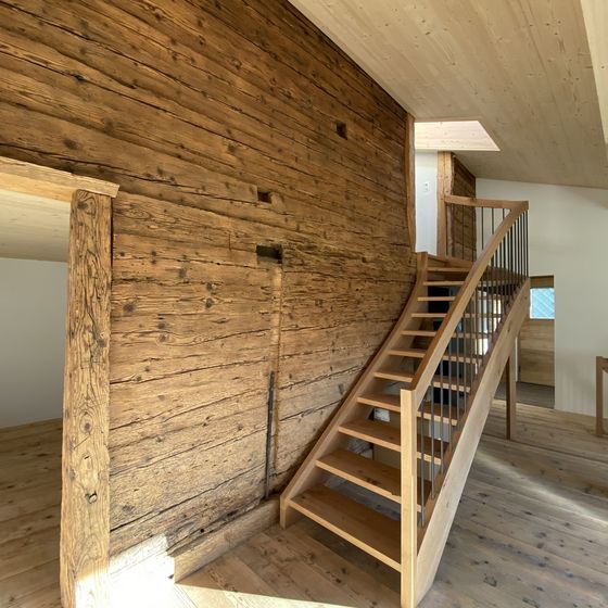 Treppenaufgang aus Holz in einem Innenraum mit rustikaler Wandverkleidung.