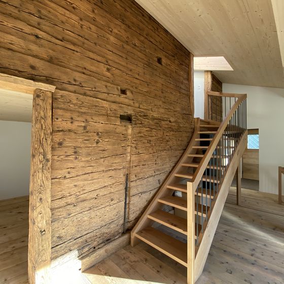 Treppenaufgang aus Holz in einem Innenraum mit rustikaler Wandverkleidung.