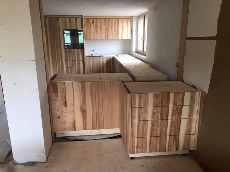 Küche im Bau mit massgefertigten Holzschränken und unverarbeitetem Holzwerk.