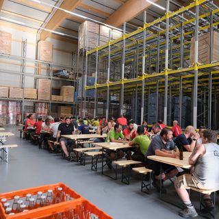Mitarbeiterpause in einem gut gefüllten Lagerraum mit Holzmaterialien und Getränken.