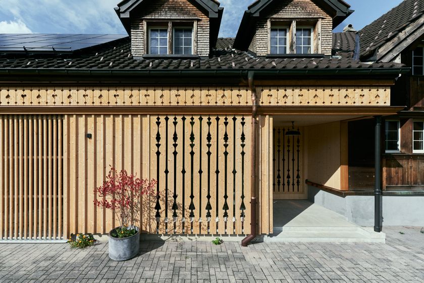 Moderne Holzfassade mit dekorativen Elementen vor traditionellem Gebäude.