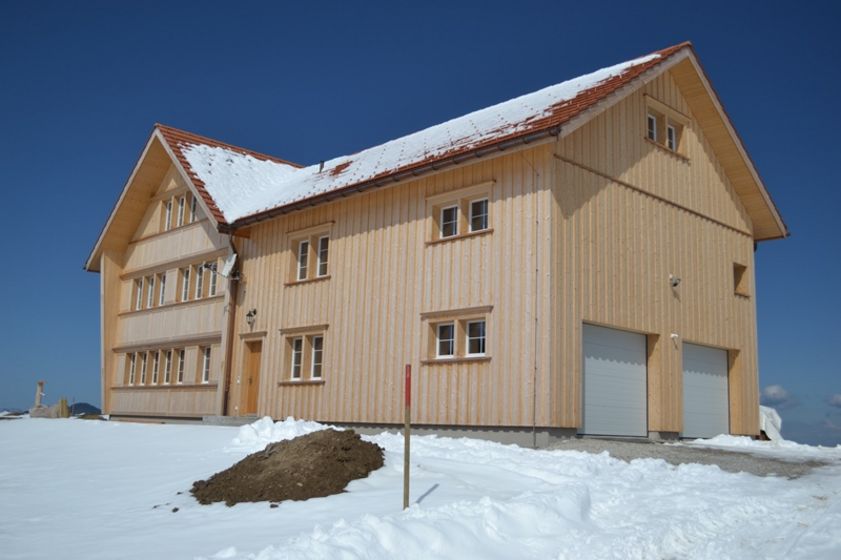 Holzhaus auf schneebedecktem Grundstück unter klarem Himmel.