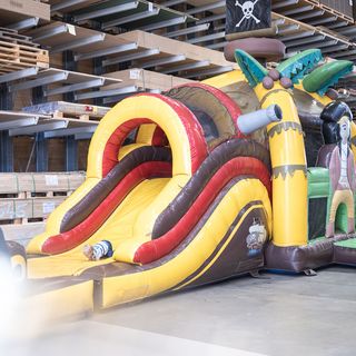 Aufblasbare Piratenrutsche in holzverarbeitender Lagerhalle mit spielendem Kind.
