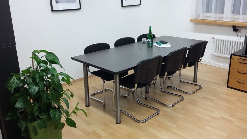 Moderner Konferenzraum mit Tisch und schwarzen Stühlen auf Holzfussboden.