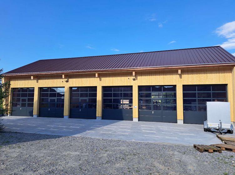 Moderne Lagerhalle aus Holz mit mehreren Garagentoren vor blauem Himmel.