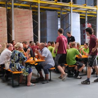 Mitarbeiterpause in einem Lager mit grossen Holzstapelungen im Hintergrund.