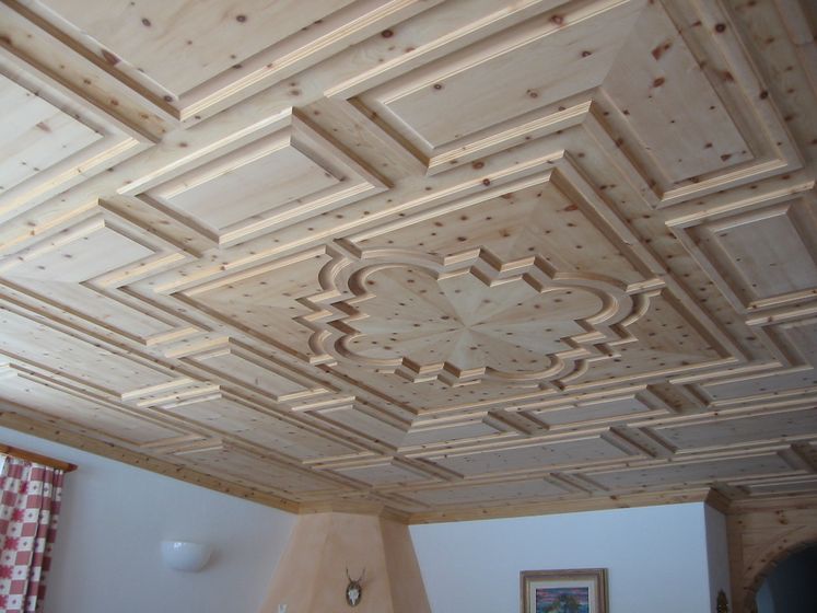 Detailreiche Holzdecke mit geometrischen Mustern in einem Wohnraum.