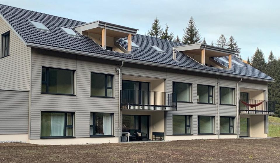 Modernes Holzgebäude mit Balkonen vor bewaldeter Kulisse.