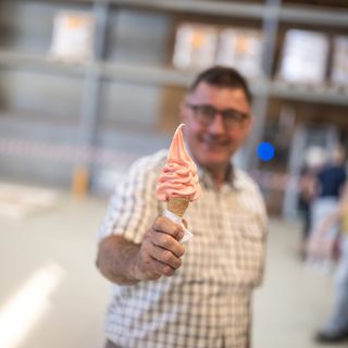 Mann hält ein Softeis in der Hand vor einem unscharfen Hintergrund in einer Lagerhalle.