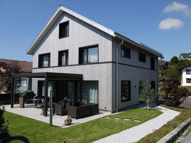 Modernes Haus mit Holzfassade und Terrasse im Grünen.
