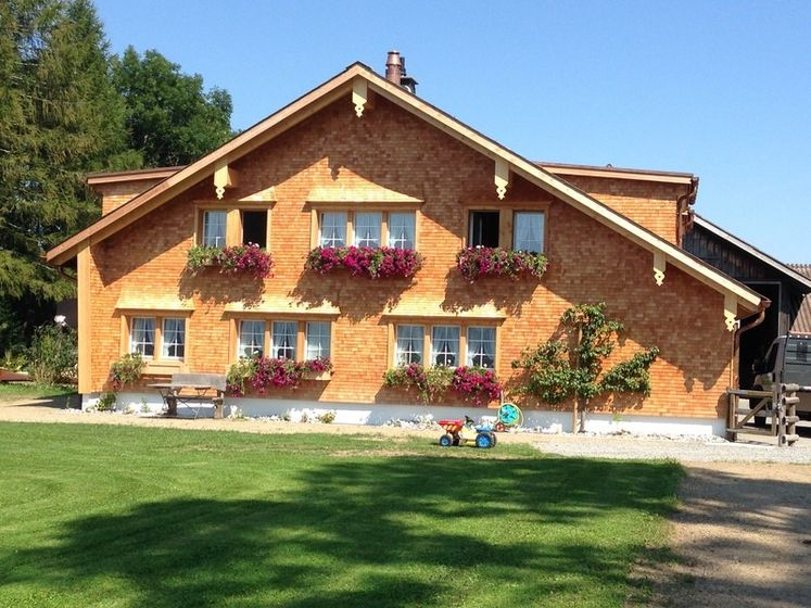 Charmantes Bauernhaus mit blühenden Fensterkästen und grüner Wiese im Vordergrund.