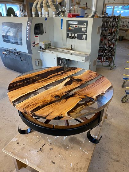 Runder Tisch mit epoxidbeschichteter Holzplatte in einer Werkstatt.