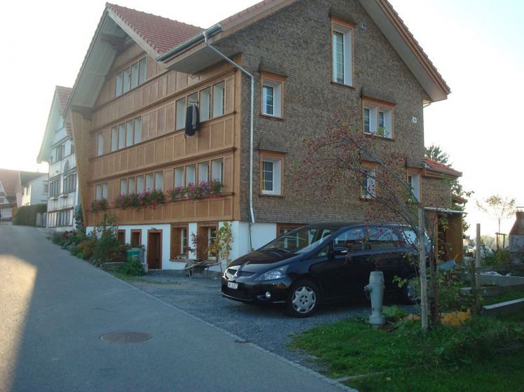 Traditionelles Haus mit Blumenkästen und einer Einfahrt mit schwarzem Auto vor der Stark AG Altstätten.
