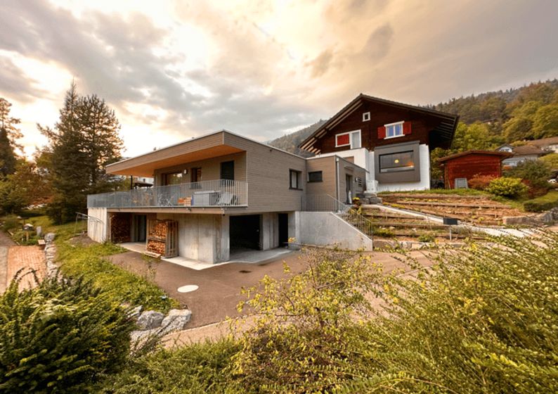 Modernes Holzhaus und traditionelles Chalet in idyllischer Landschaft bei Sonnenuntergang.