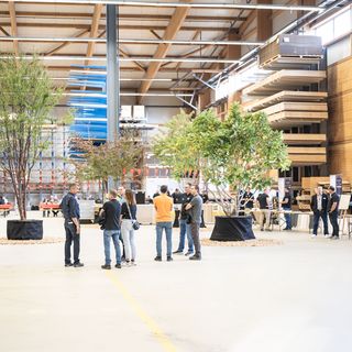 Menschen in einer Holzausstellungshalle mit Bäumen und Holzregalen.