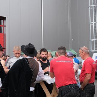 Menschen stehen um einen Stehtisch bei einer Veranstaltung vor einem modernen Gebäude.