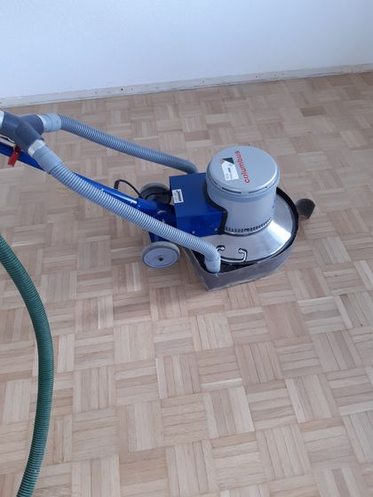 Parkettschleifmaschine auf Holzfussboden im Einsatz.