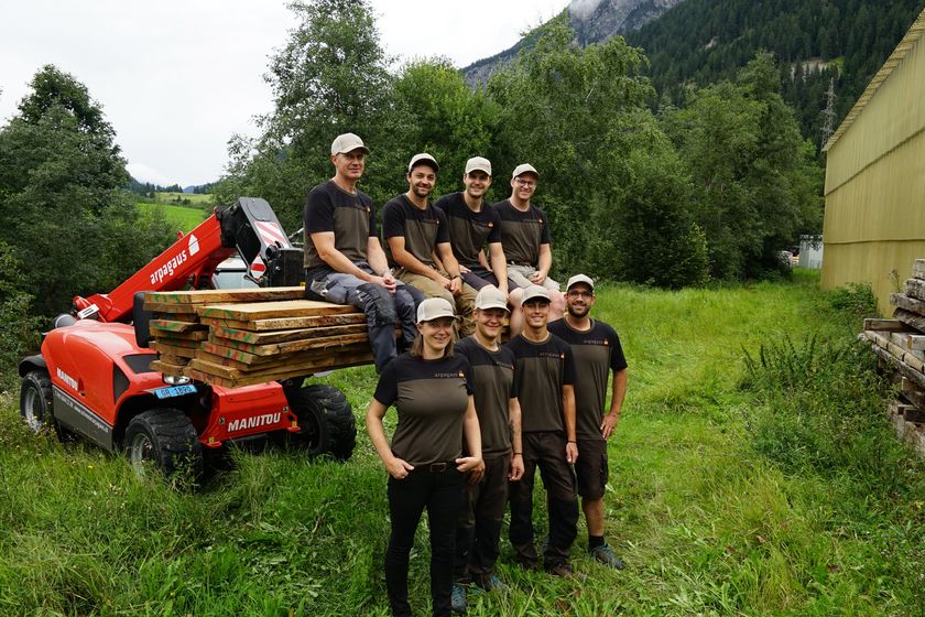 Ein Team der Stark AG posiert mit einem Holztransporter in einer grünen Landschaft.