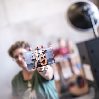 Person hält eine Broschüre mit der Zahl 75 und einem Gruppenfoto in der Hand.