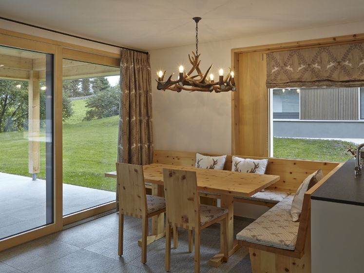 Gemütliche Essecke mit Holzinterieur und Blick auf den Garten, beleuchtet von einem Geweih-Kronleuchter.