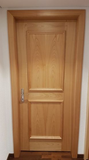 Holztür in Innenraum mit Holzmaserung und silbernem Türgriff.