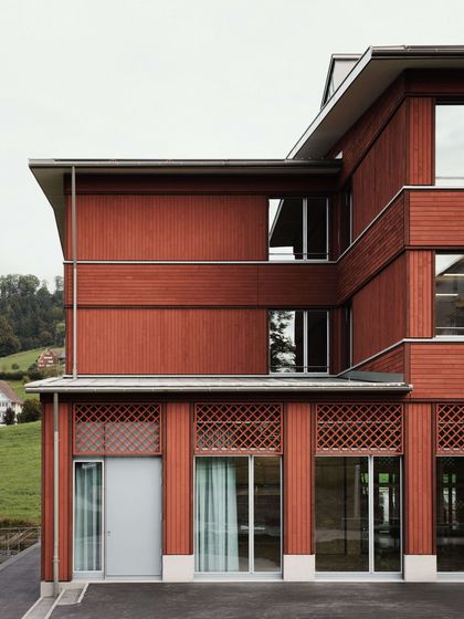 Moderne Holzfassade eines Gebäudes mit grossen Fenstern vor einer ländlichen Kulisse.
