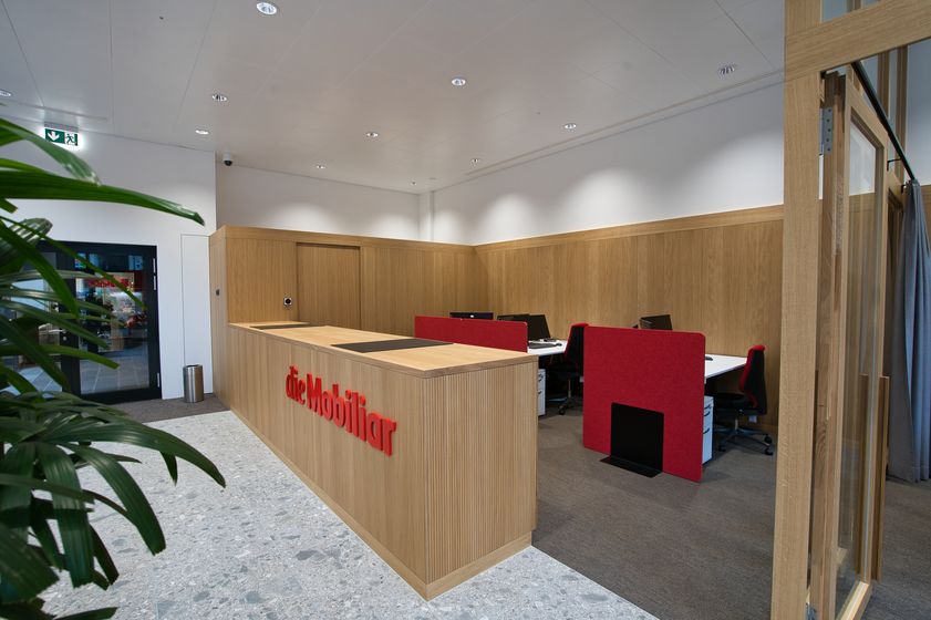 Moderner Empfangsbereich mit Holztheke und roten Bürostühlen.