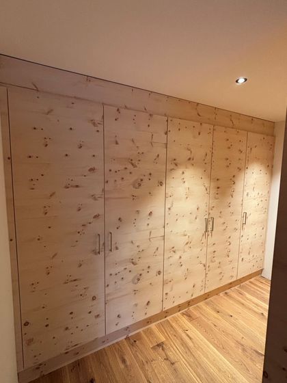 Ein eingebauter Holzschrank aus hellem Holz mit mehreren Türen, in einem Raum mit Holzboden.