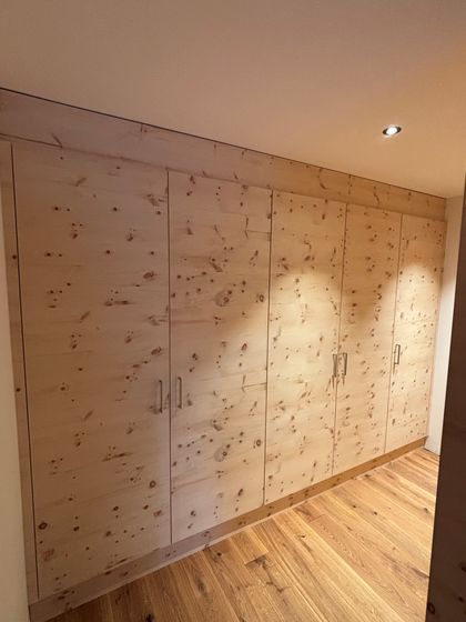 Ein eingebauter Holzschrank aus hellem Holz mit mehreren Türen, in einem Raum mit Holzboden.