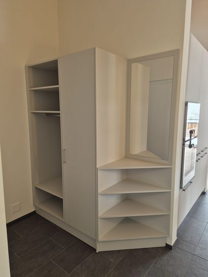 Ein moderner Einbauschrank mit offenen Regalfächern und integriertem Spiegel in einem Raum mit dunkelgrauem Fliesenboden.