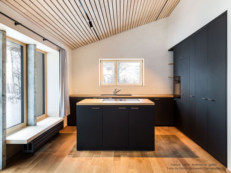 Moderne Küche mit Holzdecken und schwarzen Schränken.