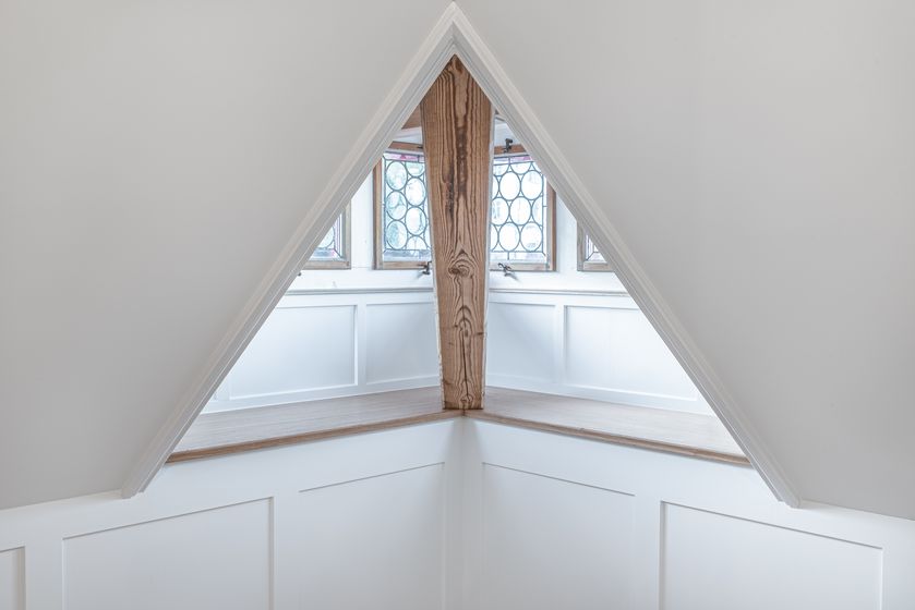 Innenansicht eines Dachraums mit Holzbalken und Fenstern.